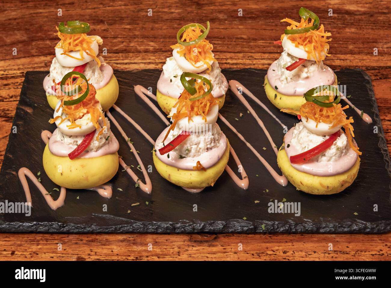 Présentation gastronomique de causa limeña avec mousse de rocoto, chips de patates douces violettes et fleurs comestibles comme décoration finale Banque D'Images