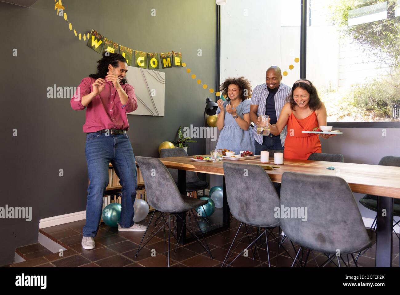 Divers amis debout autour de la table à manger à la maison, plateaux de nourriture ballons bannière de bienvenue Banque D'Images