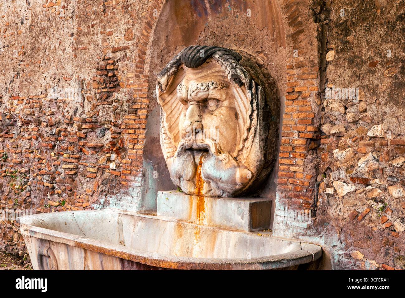 Vieille fontaine en pierre à Rome avec masque sculpté projetant de l'eau contre le mur de briques Banque D'Images