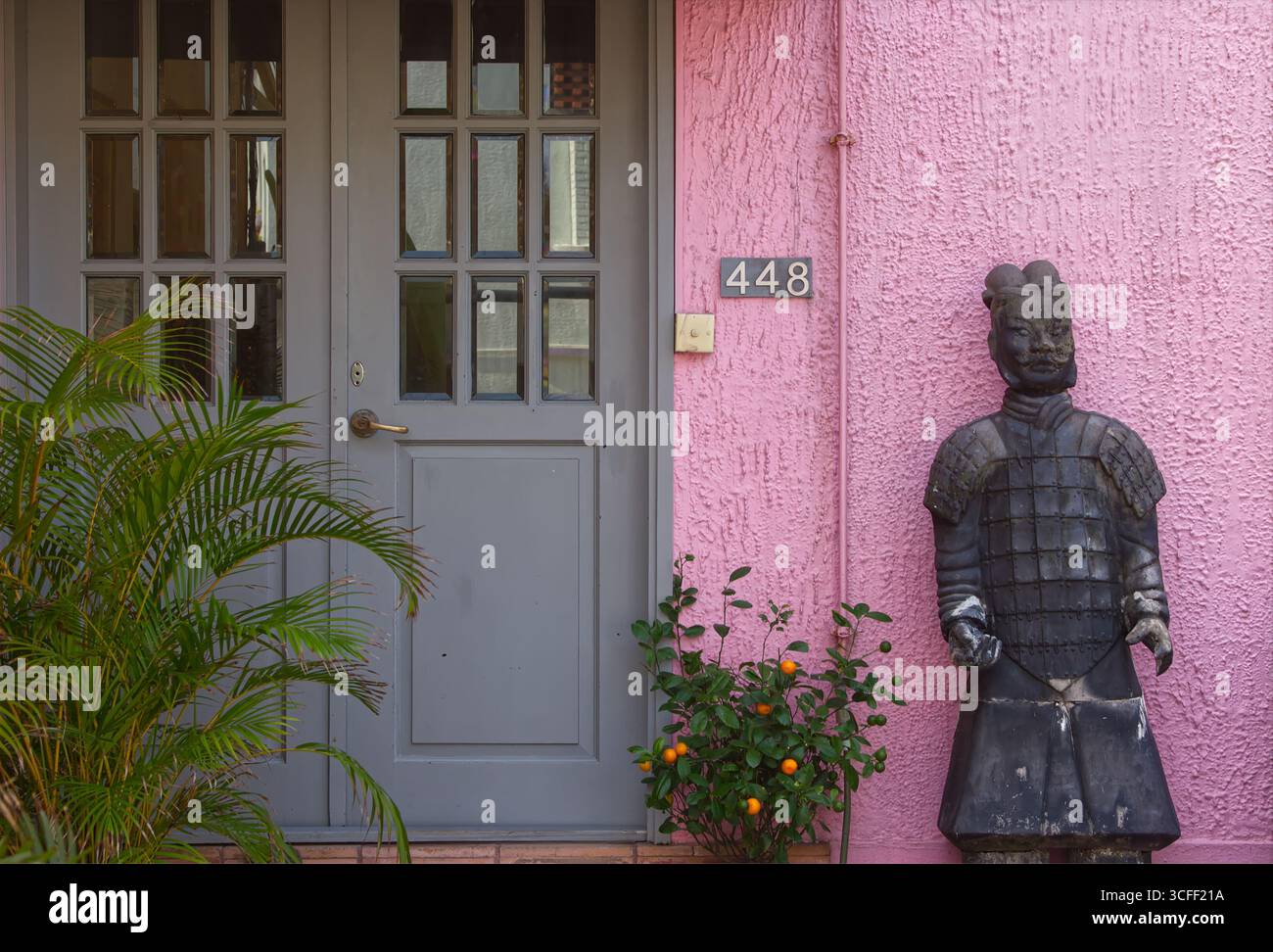 Soldat de la dynastie Qin en bronze portant une demi-armure lamellaire positionnée à l'extérieur d'une maison privée contre un mur rose et des portes à double vitrage gris Banque D'Images