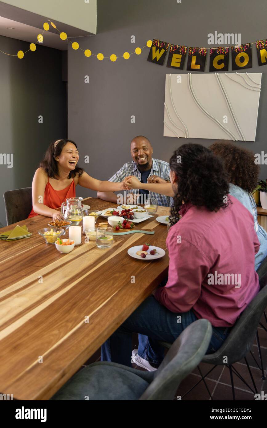 Amis riant, passant pichet et noix autour de la table dans la salle à manger sous la bannière de bienvenue Banque D'Images