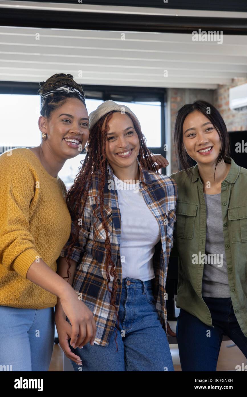 Diverses collègues féminines debout et souriantes dans le salon de bureau avec mur de briques apparentes et stores Banque D'Images