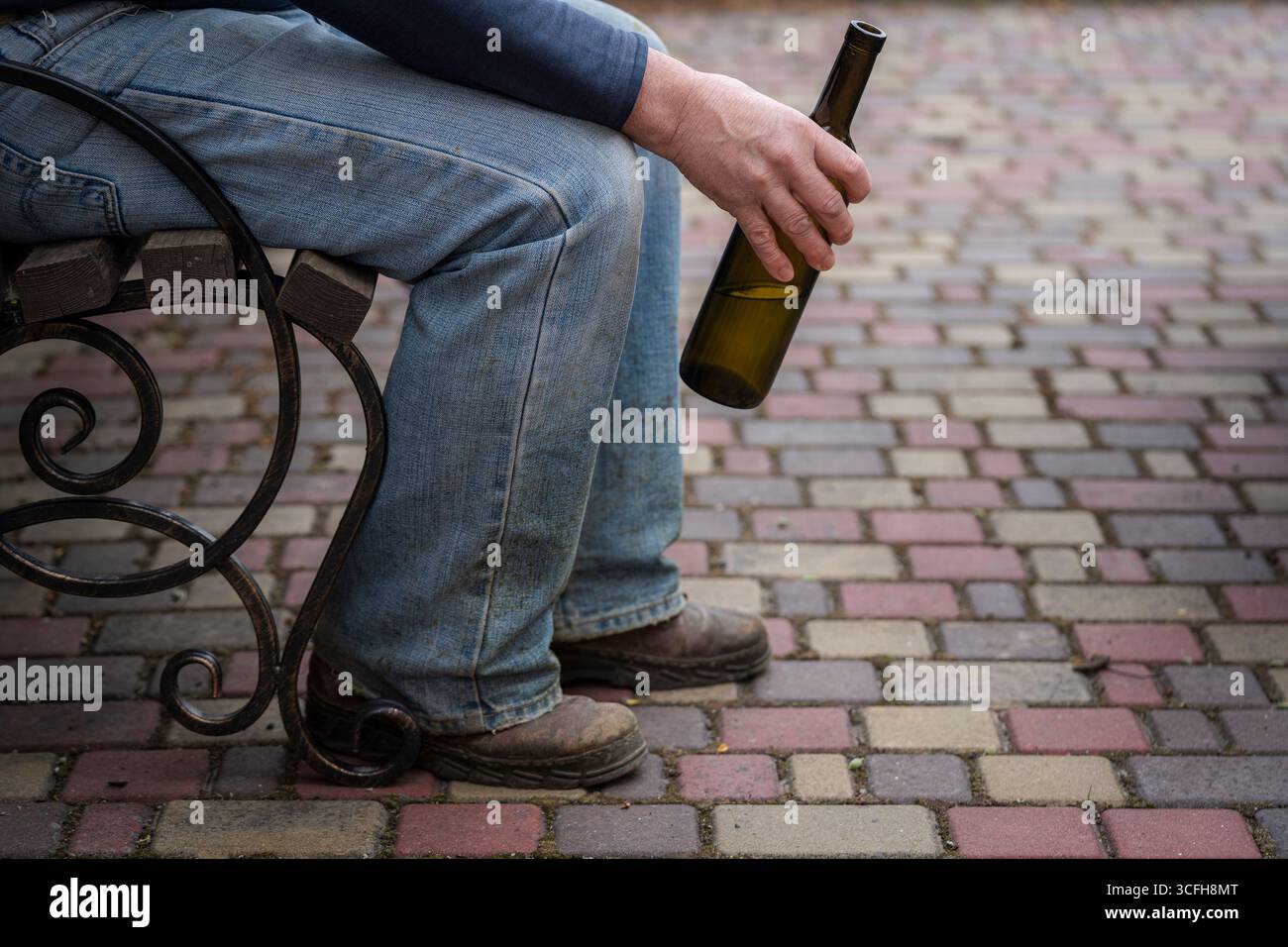 Homme solitaire est assis sur un banc et tient une bouteille de vin inachevée dans sa main, gros plan. Concept de consommation d'alcool et alcoolisme Banque D'Images