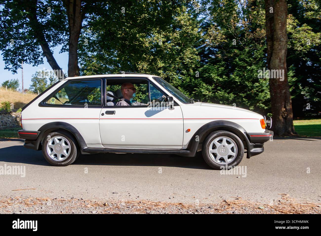 Voiture à hayon blanche vintage conduite par une journée ensoleillée avec des arbres en arrière-plan Banque D'Images