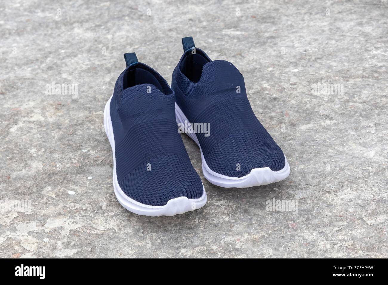 Une paire de baskets à enfiler pour femme. Chaussures confortables et à la mode pour dames, placées sur un sol en béton, vue de face. Banque D'Images