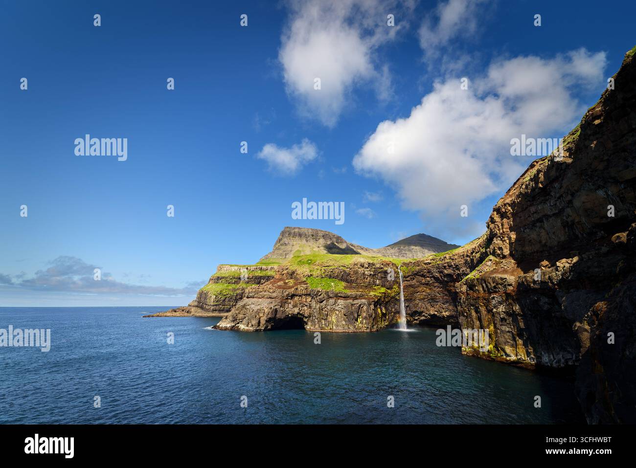 Vue panoramique de la cascade Mulafossur à Gasadalur sur l'île de Vagar, îles Féroé, tombant des falaises dans l'océan Atlantique par une journée d'été ensoleillée Banque D'Images
