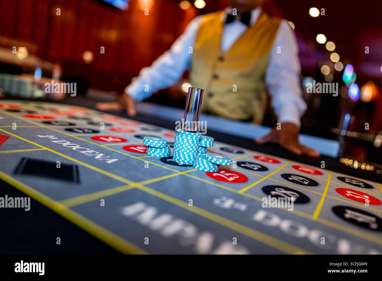 Table de roulette avec des jetons bleus empilés et un croupier en arrière-plan à l'intérieur d'un casino, symbolisant le jeu, le hasard et le divertissement. Banque D'Images