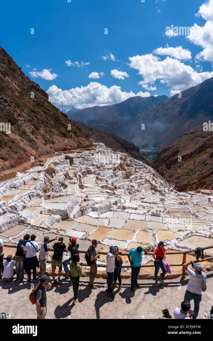 Touristes admirant les mines de sel de Maras à Cusco, Pérou. Vue panoramique sur les étangs d'évaporation en terrasses dans la Vallée sacrée, patrimoine emblématique et landmar inca Banque D'Images