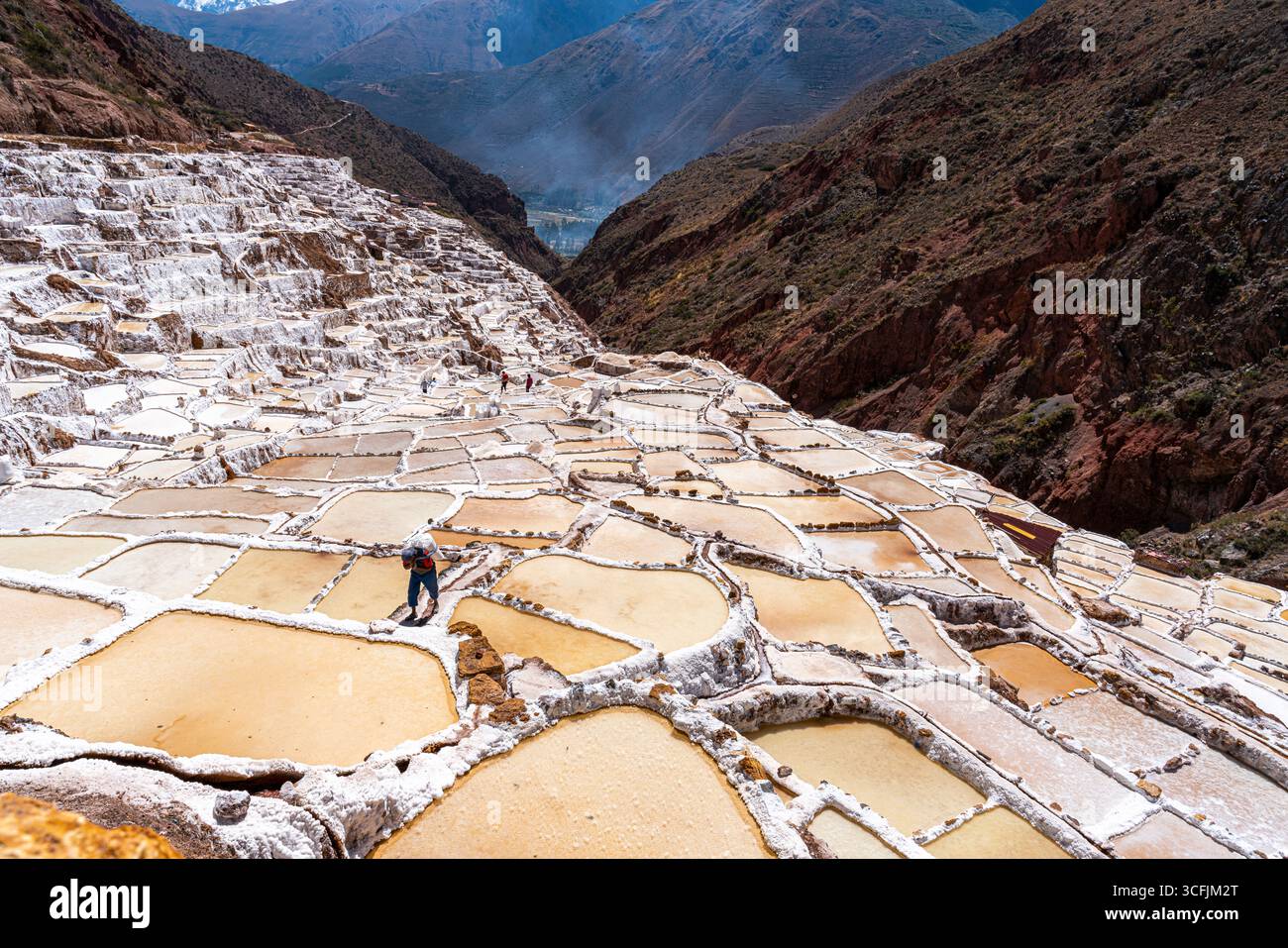Terrasses de sel de Maras à Cusco, Pérou, avec un ouvrier transportant du sel récolté. Paysage andin historique, patrimoine culturel et production traditionnelle. Banque D'Images