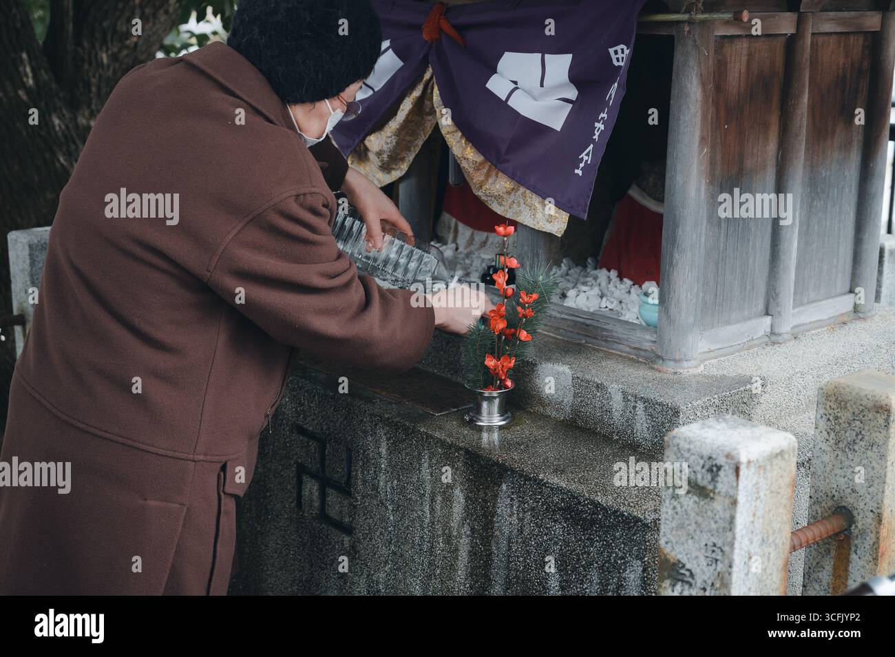 Un aîné de Kyoto verse de l'eau dans un petit sanctuaire, honorant la tradition avec des fleurs placées devant l'autel Banque D'Images
