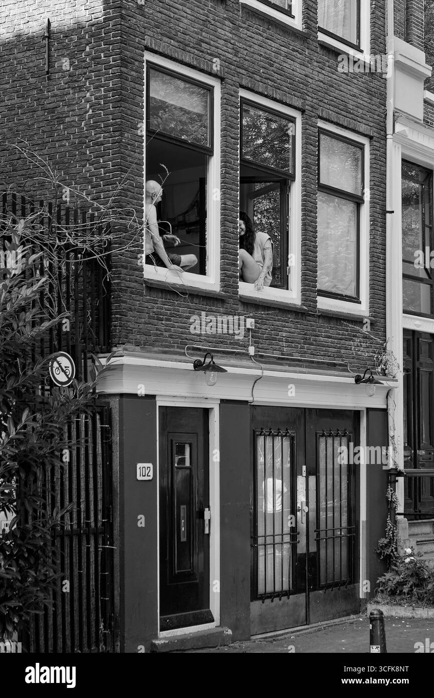 Scène de rue classique d'Amsterdam en noir et blanc avec couple dans la fenêtre de la maison hollandaise traditionnelle Banque D'Images