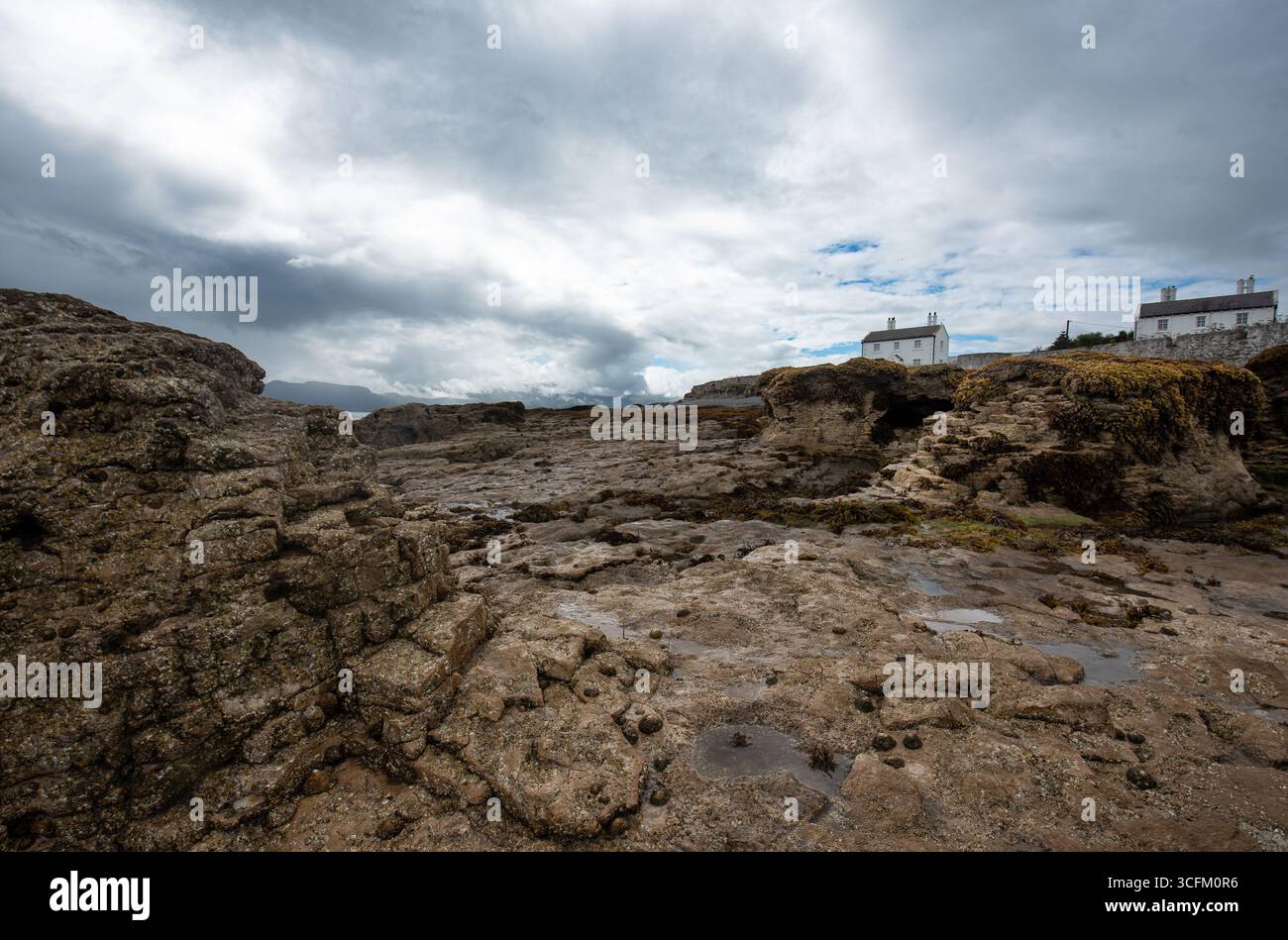 Des roches escarpées recouvertes d'algues marines sont visibles à marée basse à Penmon point, Beaumaris, alors qu'une brume marine matinale commence à se dégager au-dessus d'Anglesey. Banque D'Images