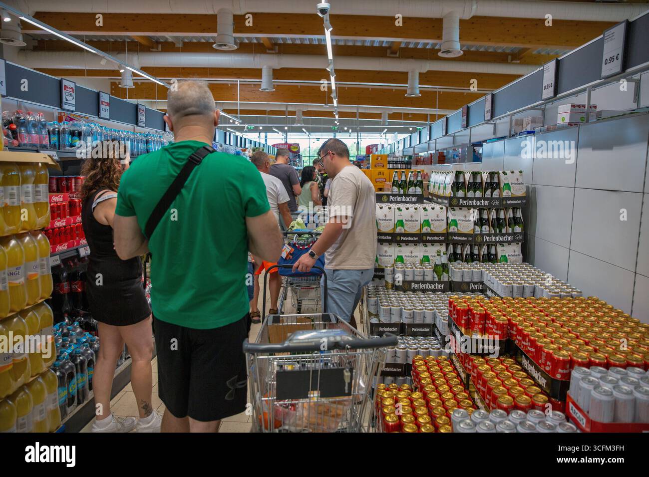 Porec, Croatie - 31 mai 2025 : les acheteurs parcourent la section des boissons dans le supermarché moderne Lidl avec des canettes de bière empilées et des bouteilles. Épicerie très fréquentée Banque D'Images