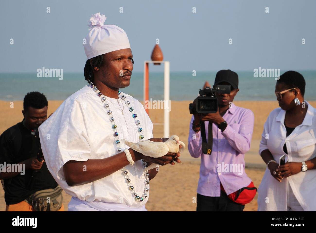 Ouidah, Bénin. 23 août 2025. Un homme tient une colombe blanche symbolisant la paix lors de la commémoration de la Journée internationale du souvenir de la traite négrière et de son abolition, à Ouidah, Bénin, le 23 août 2025. POUR ALLER AVEC 'Bénin marque la journée internationale de commémoration de la traite des esclaves et de l'abolition' crédit : Séraphin Zounyekpe/Xinhua/Alamy Live News Banque D'Images