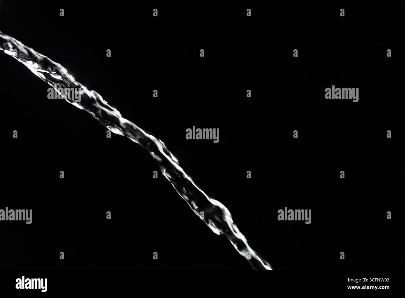 Flot d'eau limpide coulant sur fond noir isolé, gros plan. Jet transparent d'eau propre en cascade contre un fond sombre Banque D'Images