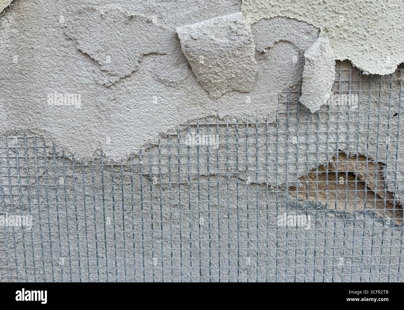 Gros plan d'un mur de plâtre détérioré avec des couches pelables et un treillis de renforcement visibles Banque D'Images