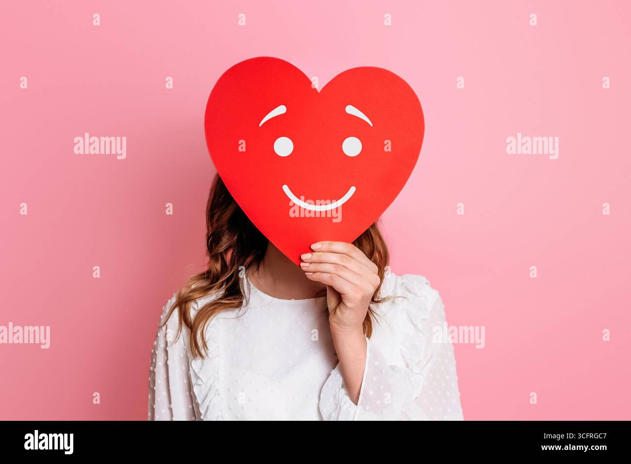 fille tenant le coeur de papier avec le visage heureux smiley isolé sur fond rose. Tomber amoureux concept Banque D'Images