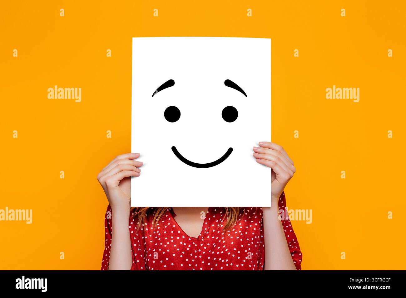 Fille tenant une affiche en papier avec un smiley joyeux isolé sur fond orange Banque D'Images