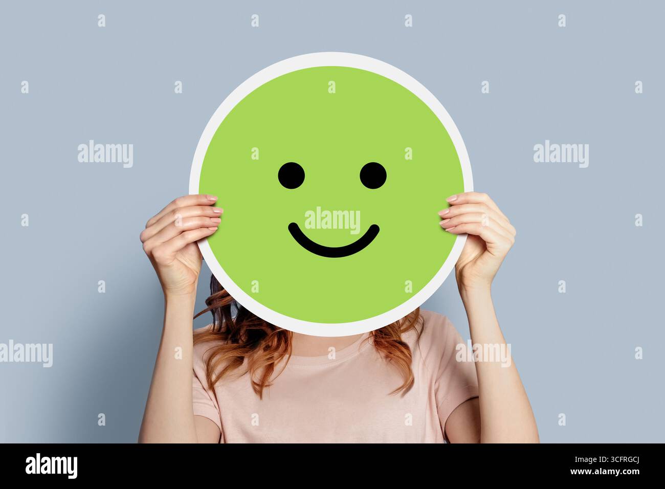 Fille tenant une affiche en papier avec un smiley joyeux isolé sur fond gris Banque D'Images