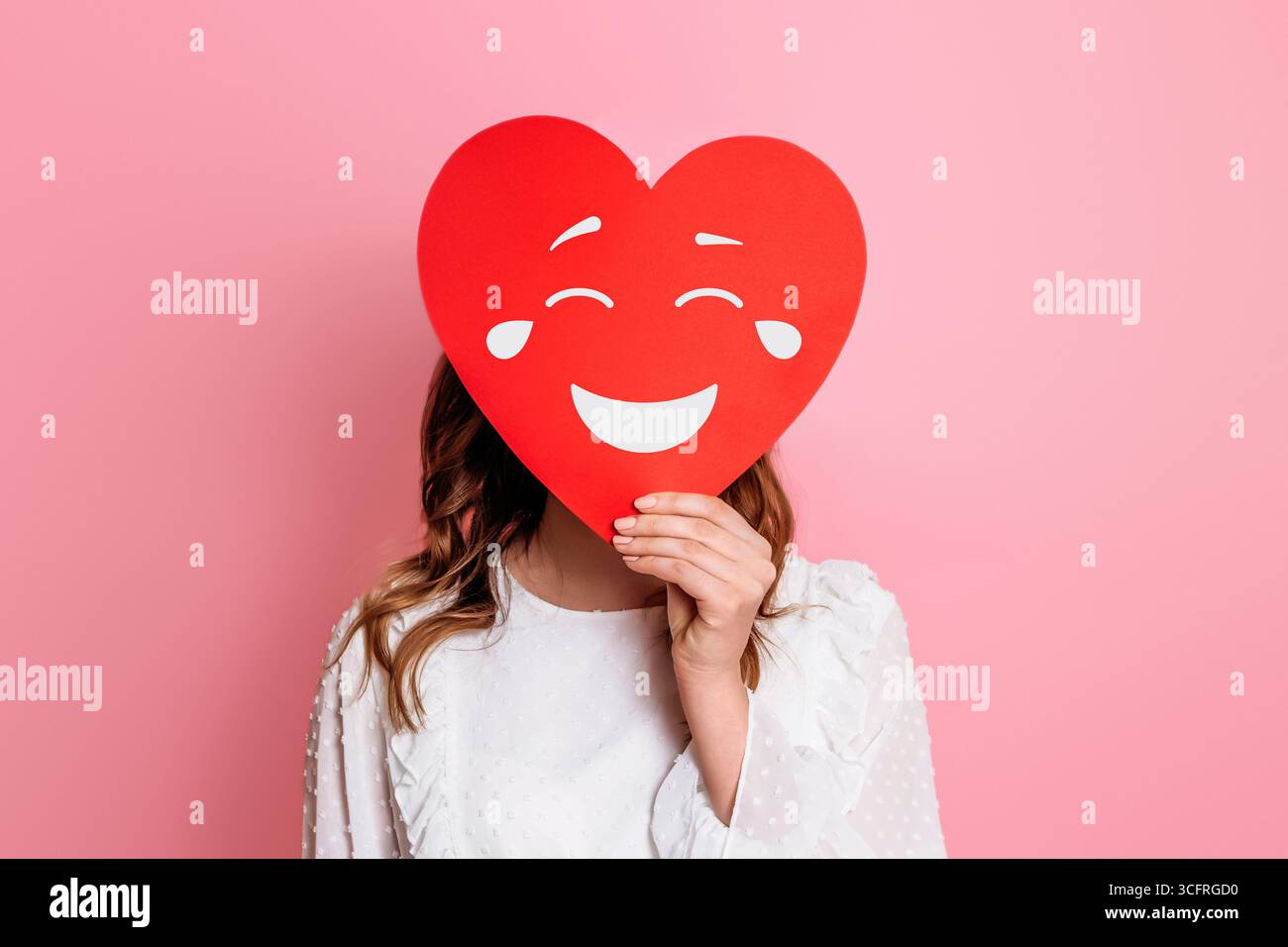 fille tenant le coeur de papier avec le visage riant smiley isolé sur fond rose. concept humour Banque D'Images