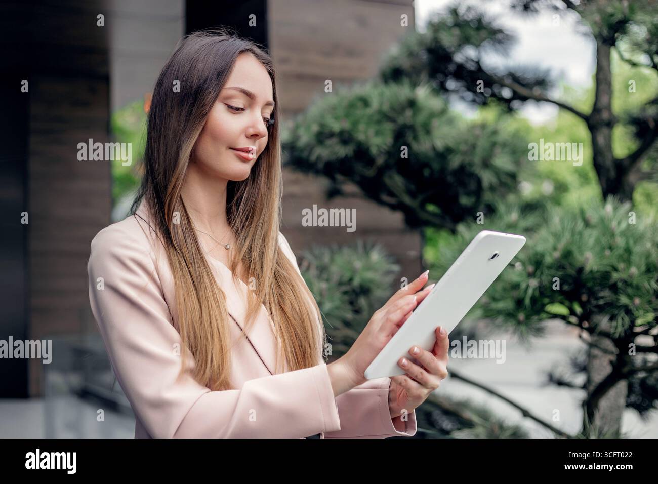 Belle femme d'affaires caucasienne souriante debout et regardant l'écran de la tablette. debout dans la rue près de l'immeuble de bureaux Banque D'Images