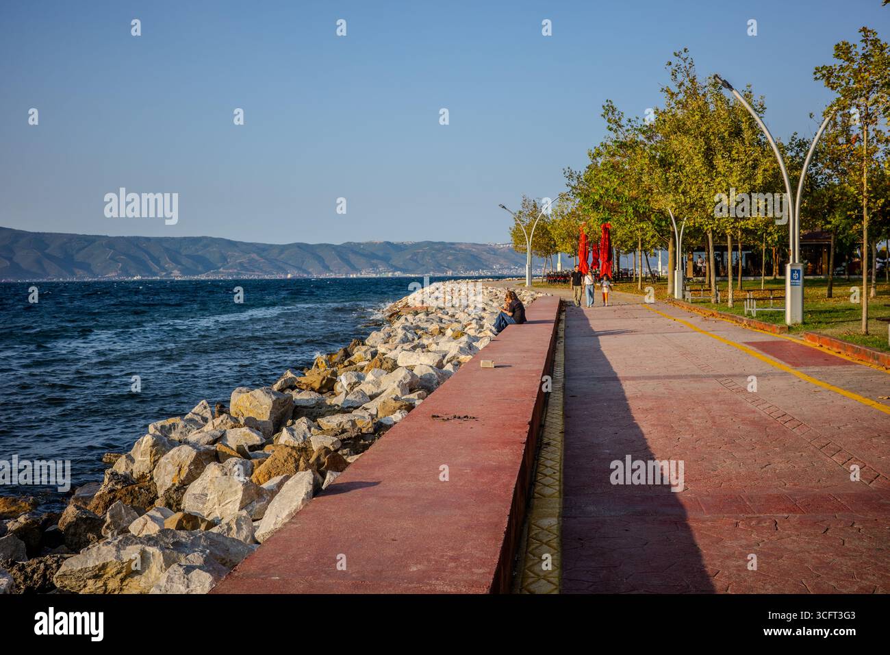 Les gens se promènent et se détendent le long d'une promenade au bord de l'eau à côté des rochers brise-lames sur la mer de Marmara. Karamürsel, Kocaeli, Türkiye – 23 août 2025. Banque D'Images