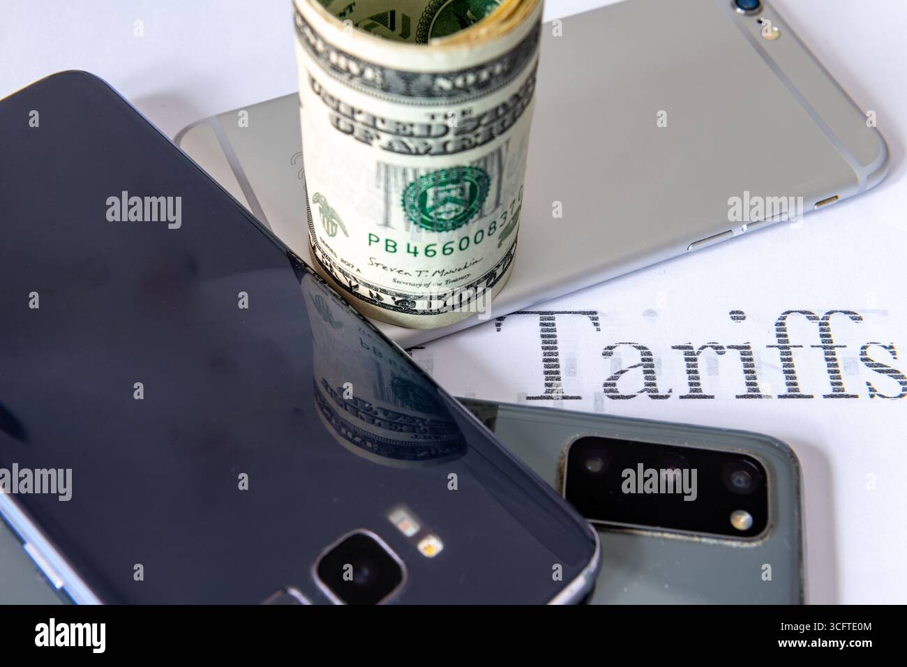 Téléphones intelligents et un rouleau de billets en dollars américains sur fond blanc avec le mot imprimé tarifs. Un concept américain de taxe tarifaire électronique à la consommation. Banque D'Images