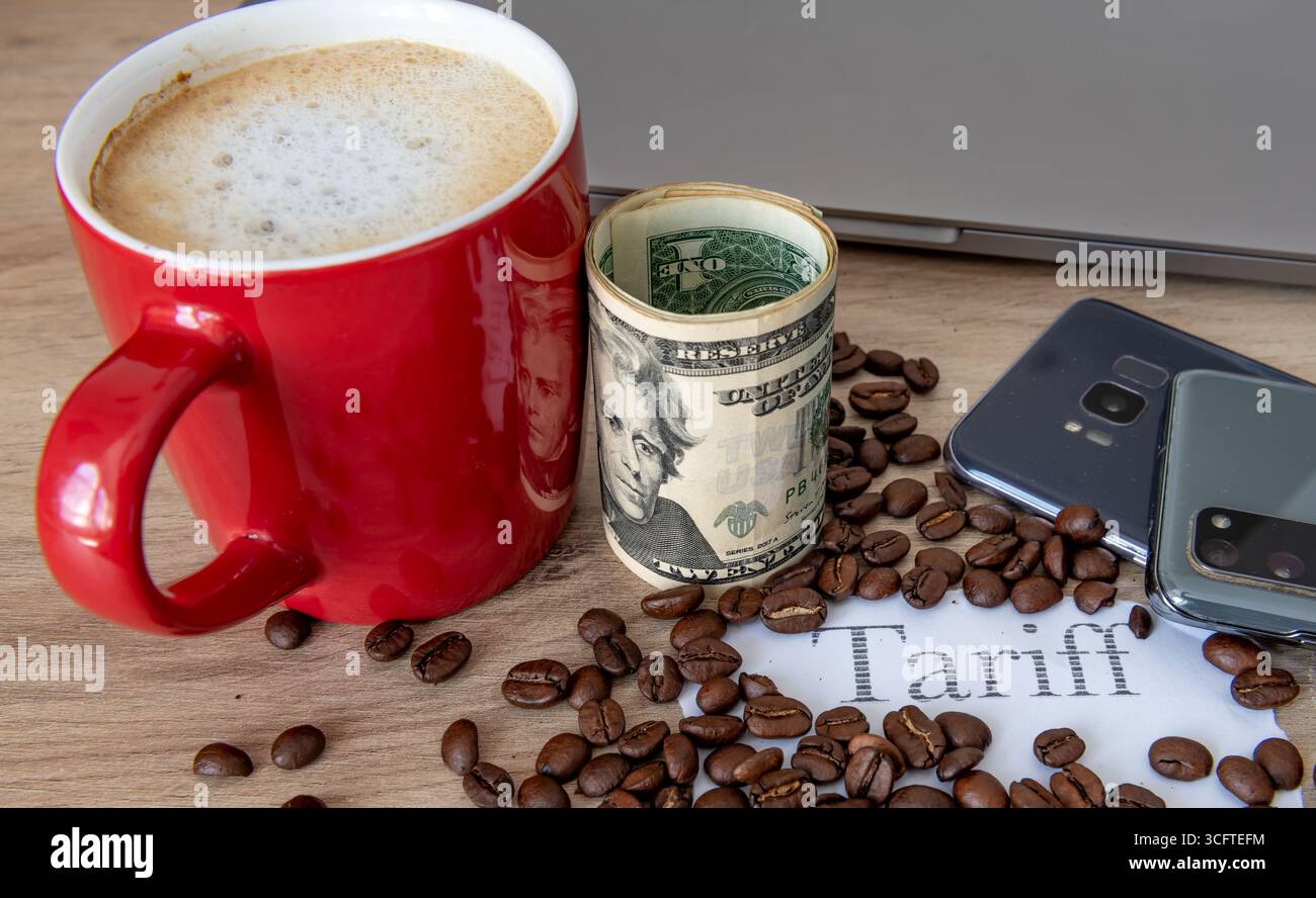 Une tasse de café, des grains de café, un rouleau de billets en dollars américains, le mot imprimé tarif et des produits électroniques sur une table. Un concept de taxe tarifaire américaine. Banque D'Images