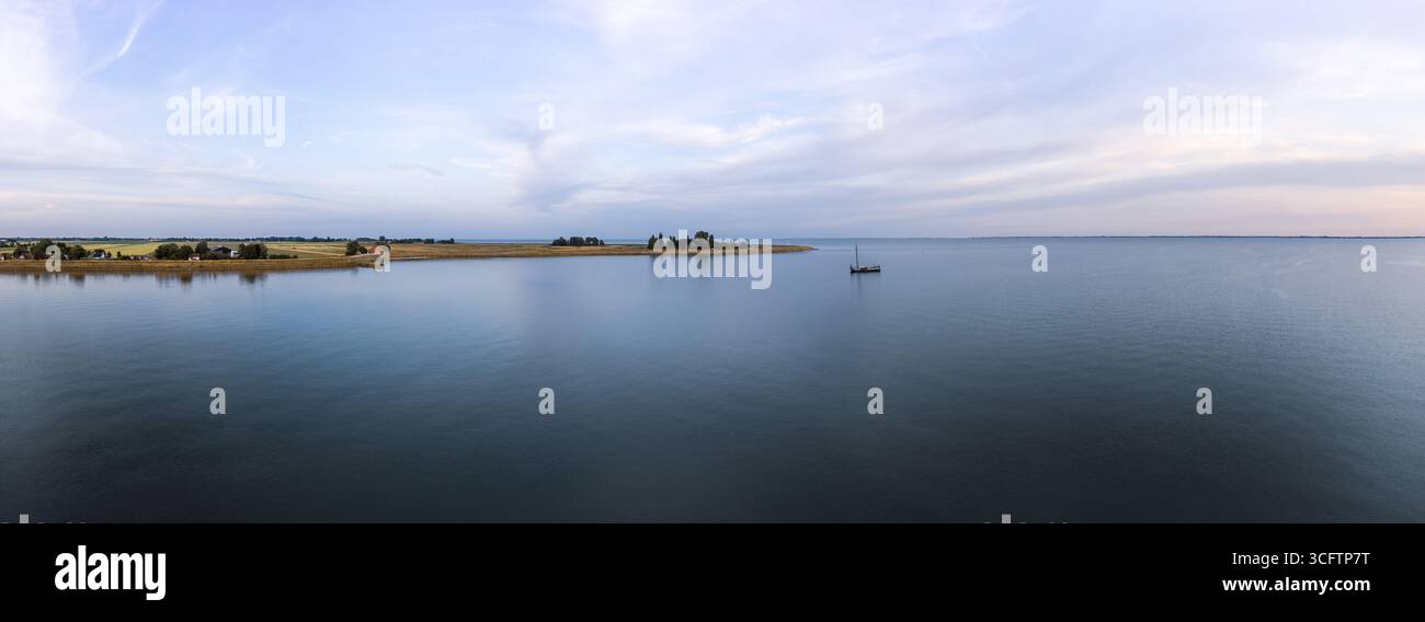 Vue tranquille en soirée sur un bateau tjalk avec des voiles roulées sur le lac Markermeer aux pays-Bas, entouré par l'eau sereine et un horizon calme Banque D'Images