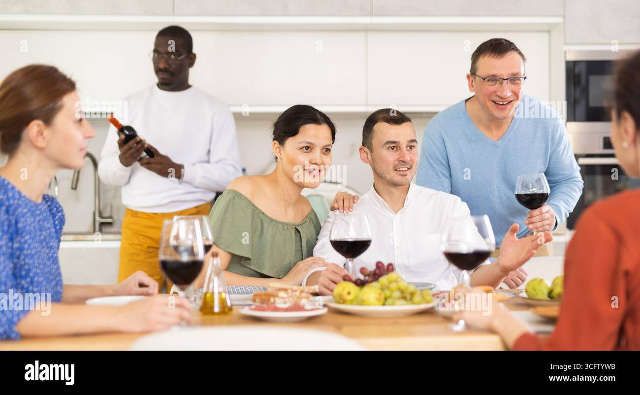 Les compagnons se sont rassemblés autour d’une table festive, participant à des discussions animées et dégustant les délices du vin rouge Banque D'Images