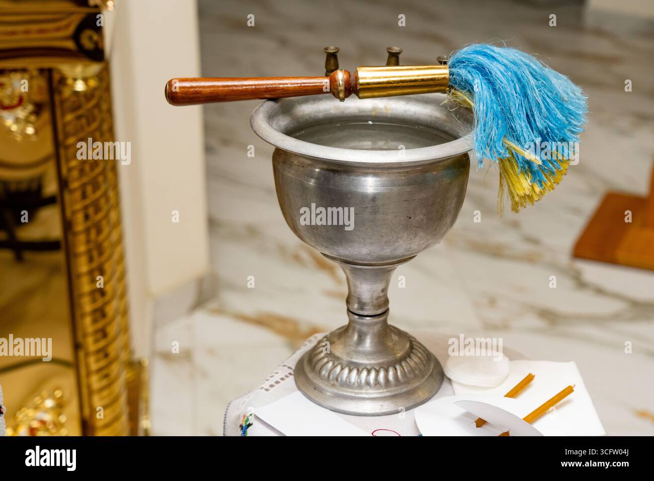 Gros plan d'un récipient d'eau bénite en métal avec un aspergillum traditionnel (brosse) placé sur le dessus, utilisé pour asperger l'eau bénite pendant le cérémonial religieux Banque D'Images