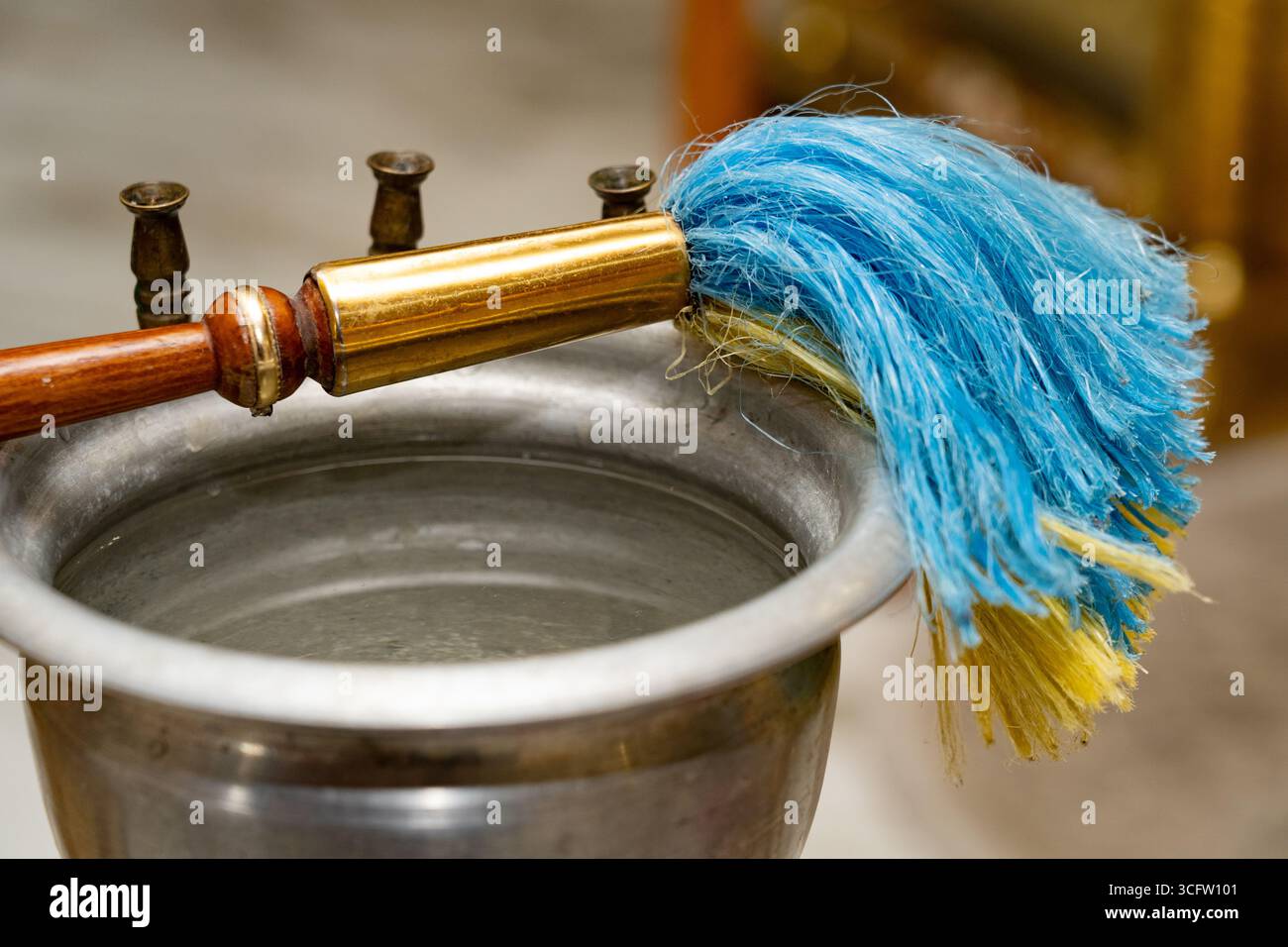 Gros plan d'un récipient d'eau bénite en métal avec un aspergillum traditionnel placé sur le dessus, utilisé pour arroser l'eau bénite pendant les cérémonies religieuses insi Banque D'Images