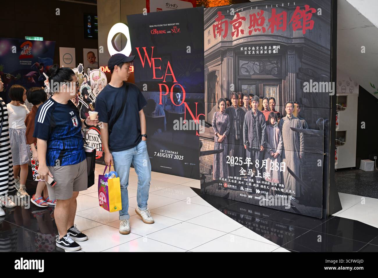 Kuala Lumpur, Malaisie. 24 août 2025. Les gens regardent une affiche de "Dead to Rights" à Kuala Lumpur, Malaisie, le 24 août 2025. La première malaisienne de « Dead to Rights », un film historique chinois sur le massacre de Nanjing en 1937, a eu lieu dimanche à Kuala Lumpur, ce qui a suscité un vif écho auprès du public. POUR ALLER AVEC 'film chinois sur le massacre de Nanjing en première en Malaisie' crédit : Cheng Yiheng/Xinhua/Alamy Live News Banque D'Images
