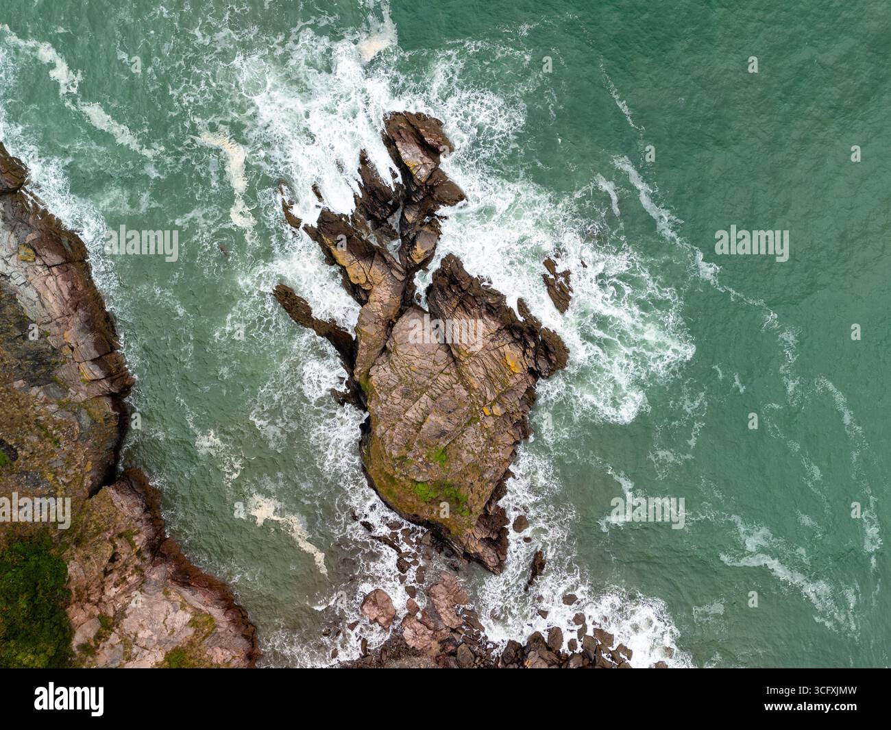 Vue aérienne des vagues de l'océan s'écrasant contre une falaise rocheuse, créant de la mousse blanche et une scène dynamique de la puissance de la nature Banque D'Images