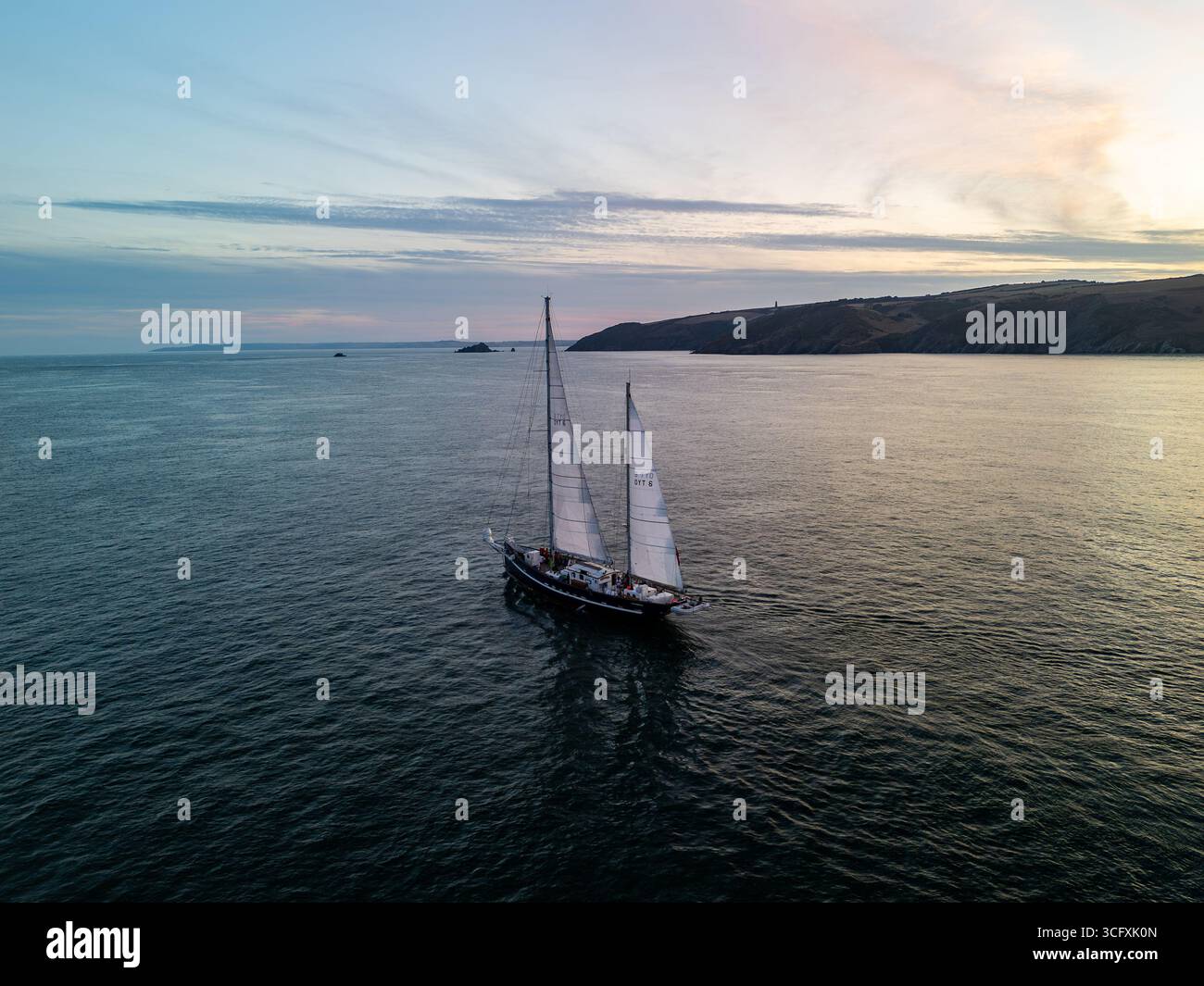 Ketch naviguant gracieusement à travers la mer au coucher du soleil, capturant une vue aérienne de la côte animée et des eaux tranquilles Banque D'Images
