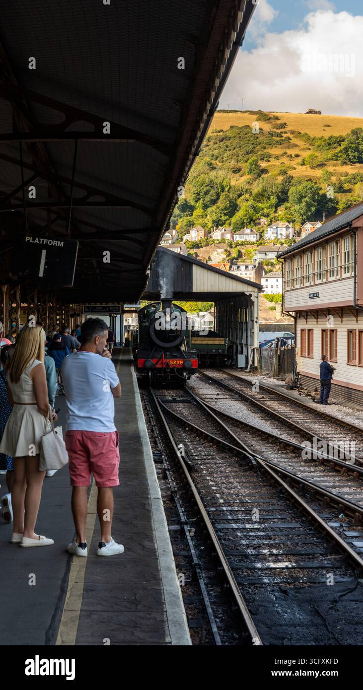 Touristes attendant sur le quai un pour le train à vapeur arrivant à la gare de Kingswear dans le Devon, Angleterre, avec des collines en arrière-plan Banque D'Images