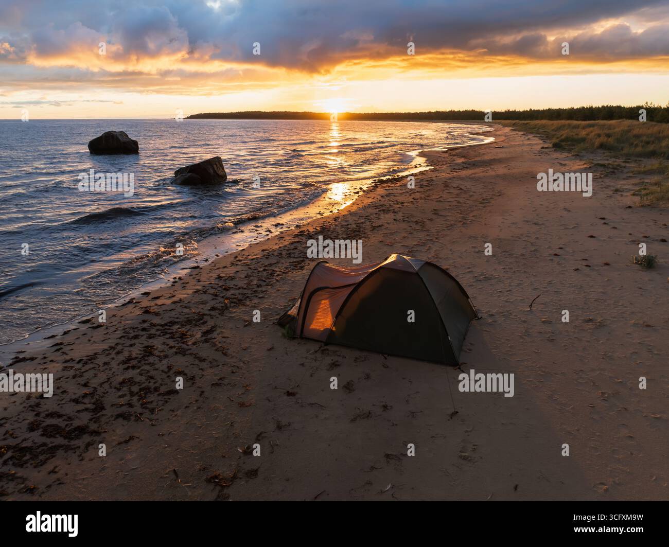 Une tente illuminée sur une plage de sable estonienne lors d'un spectaculaire coucher de soleil doré sur la magnifique mer Baltique. Banque D'Images