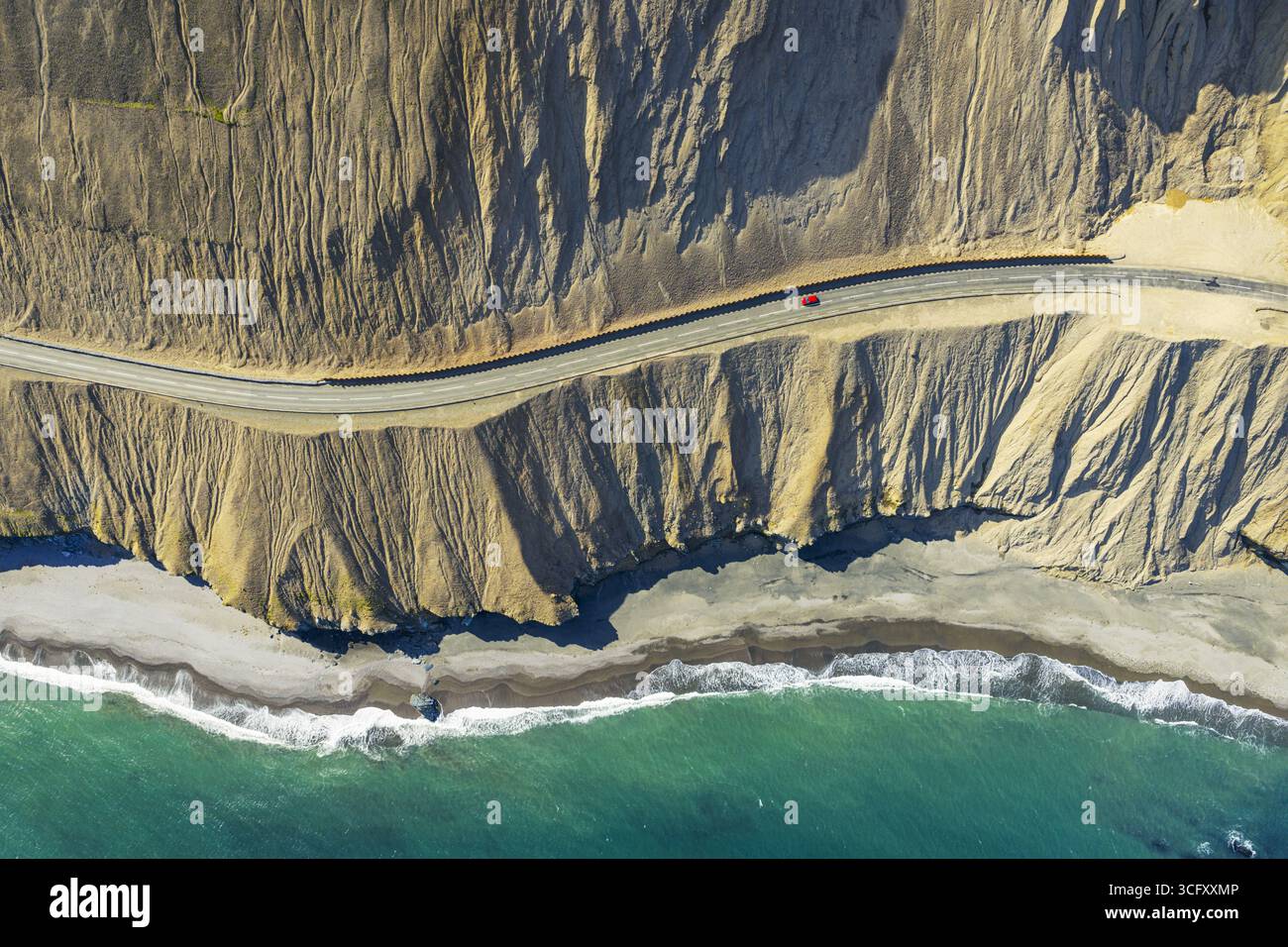Vue aérienne d'une route sinueuse serpente le long de la côte accidentée, où les falaises ocres rencontrent la mer turquoise dans un spectacle à couper le souffle de la nature artis Banque D'Images