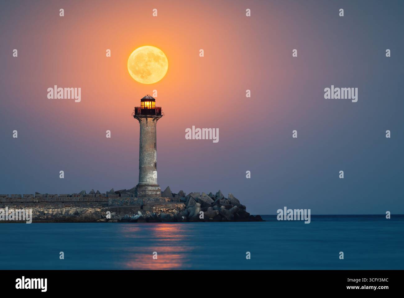 Paysage crépusculaire de pleine lune au-dessus de l'horizon de la mer et phare d'éclairage de la côte Banque D'Images