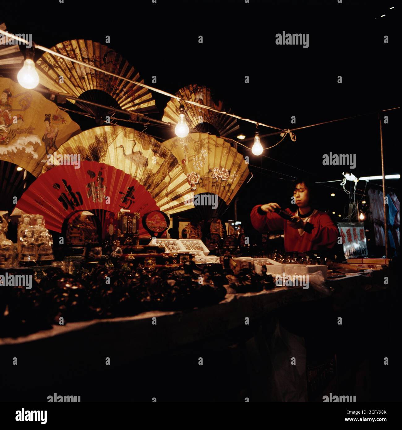 Ein Verkaufsstand mit dekorativen Fächern und souvenirs BEI Nacht, beleuchtet von Glühbirnen. Hong Kong, um 1980. Banque D'Images