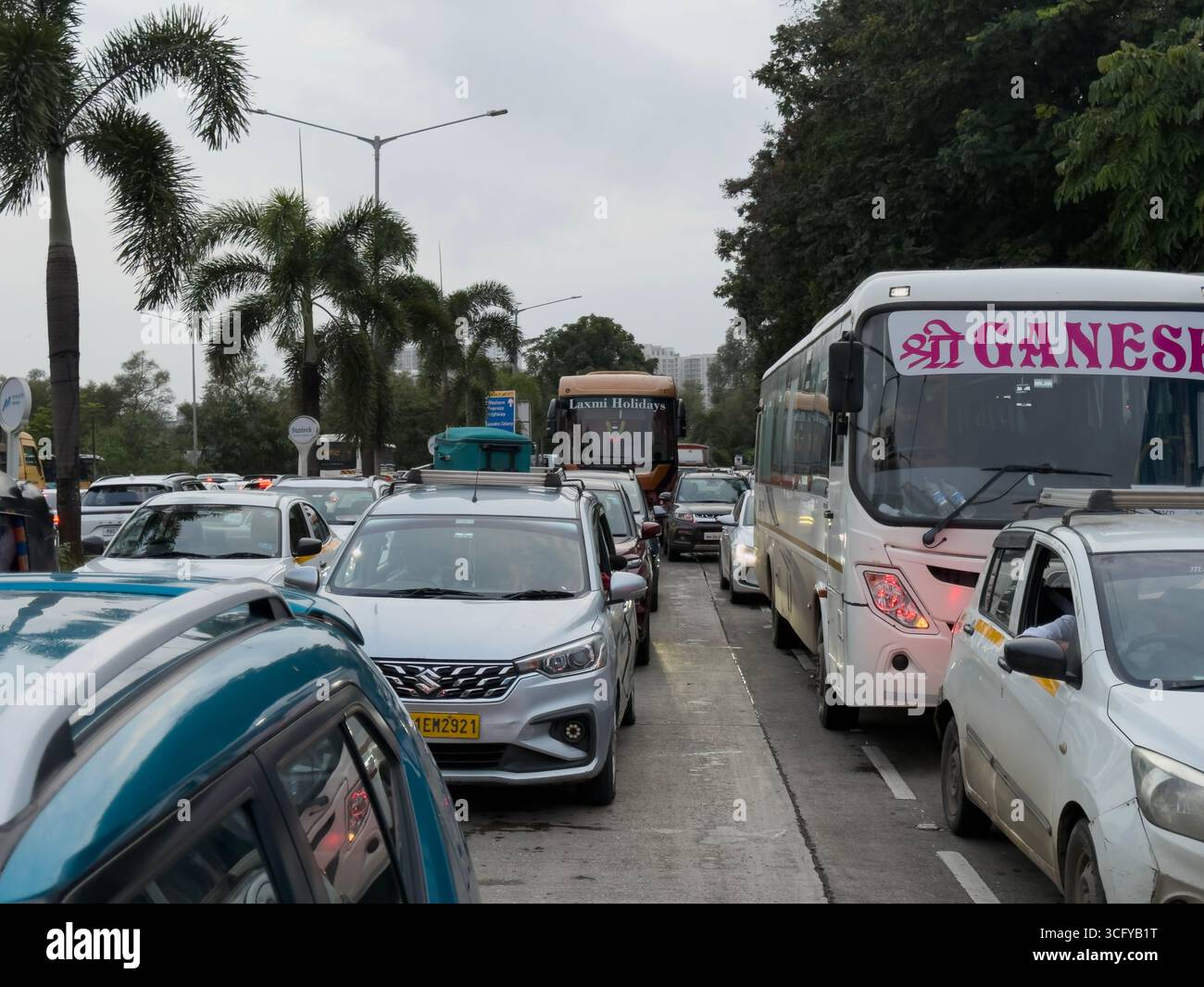 Cette image illustre la circulation dense sur une route urbaine, avec plusieurs voitures, taxis et deux grands bus, dont l’un marqué « Shri Ganesh », avec des palmiers A. Banque D'Images
