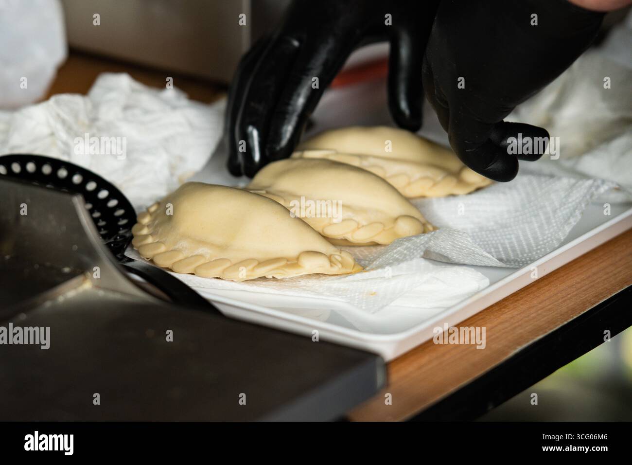 Une personne portant des gants noirs prépare des empanadas, des pâtisseries ou frites composées de pâtisseries et de farces Banque D'Images