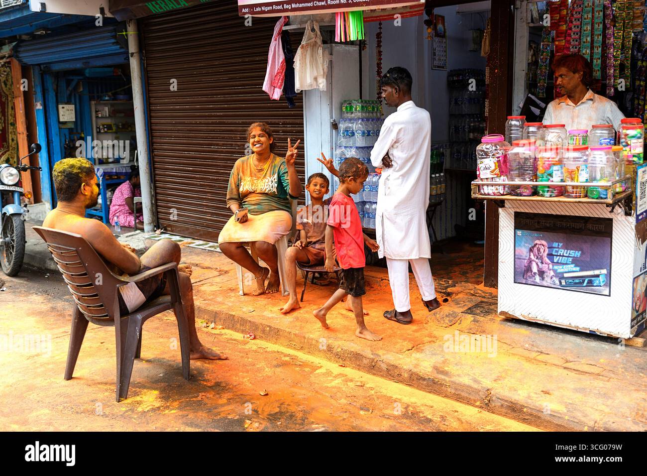 Famille locale avec des couleurs sur leurs visages célébrant le festival holi, festival des couleurs assis près d'un magasin de rue, mumbai, inde, poudre sur le sol Banque D'Images