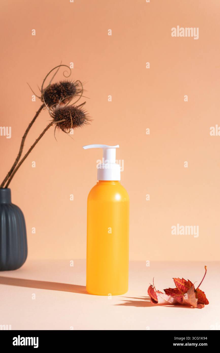 Bouteille cosmétique jaune, feuille d'automne et fleurs sèches dans un vase sur fond orange clair. Concept cosmétique naturel. Gros plan. Banque D'Images