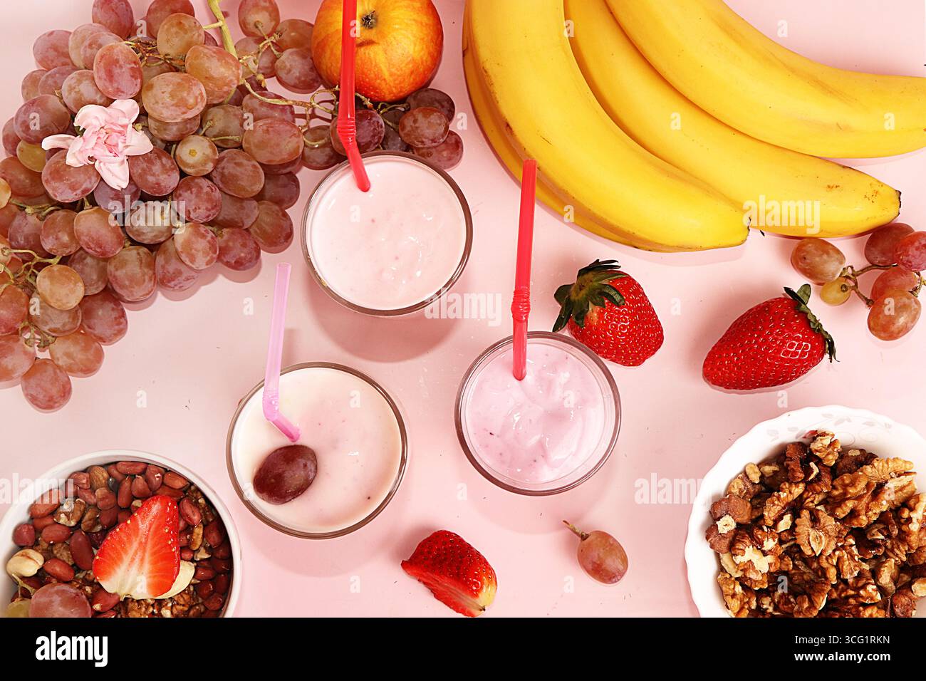 Smoothies à la fraise et à la banane, granola, baies fraîches, bananes et raisins sur un fond rose ensoleillé. Le concept de nourriture saine et naturelle. Usefu Banque D'Images