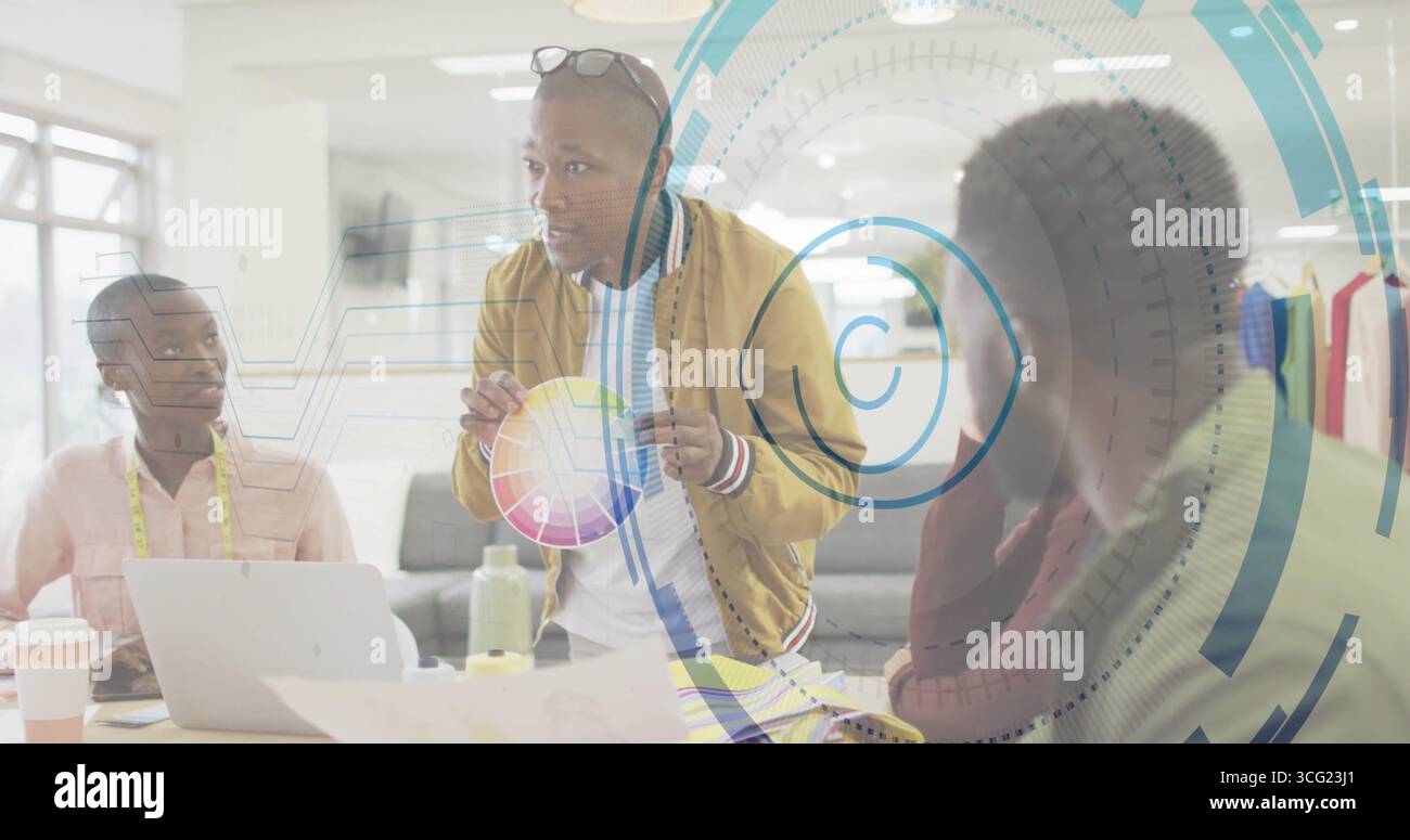 Directeur créatif penchant tenant un tableau de roue de couleur imprimé autour de la table de réunion, avec ordinateur portable Banque D'Images