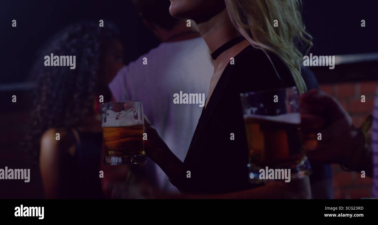 Bavardez des amis portant un collier de choker tenant des tasses à bière en verre au bar la nuit contre un mur de briques Banque D'Images