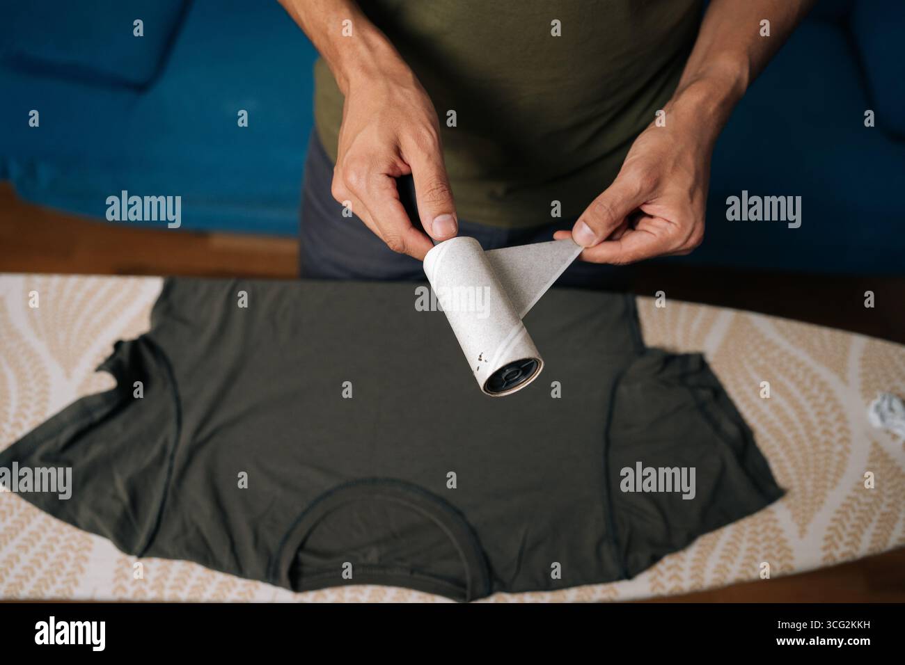 Gros plan de dessus de l'homme décollant la couche usagée de rouleau à peluches collantes, se préparant à nettoyer les vêtements de la poussière, des cheveux et des fibres, en s'assurant que les vêtements restent Banque D'Images