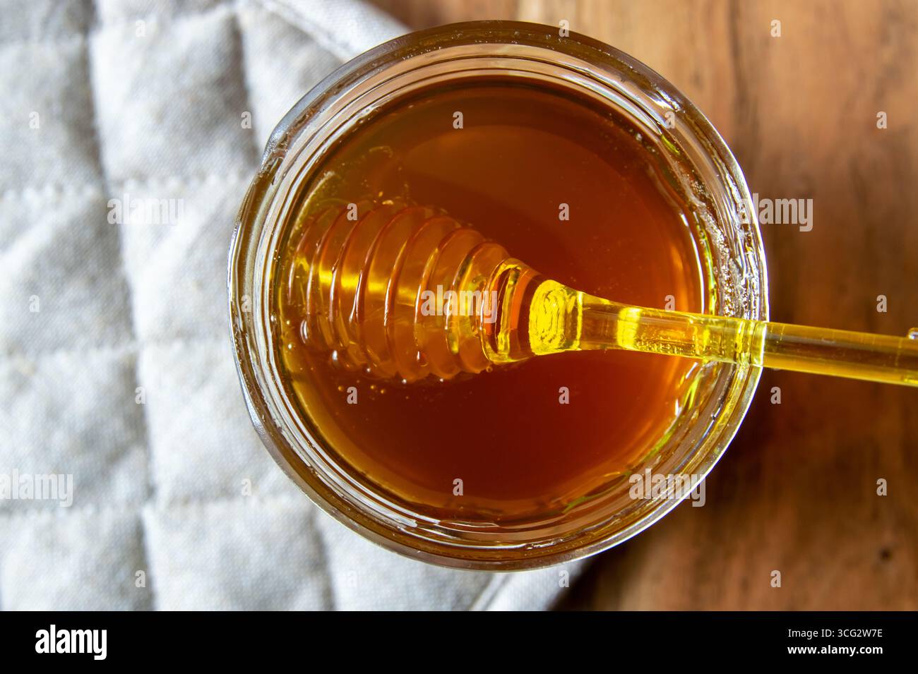 Miel grand pot en verre avec nid d'abeille et cuillère jaune rester sur la table en bois avec serviette rustique. Banque D'Images
