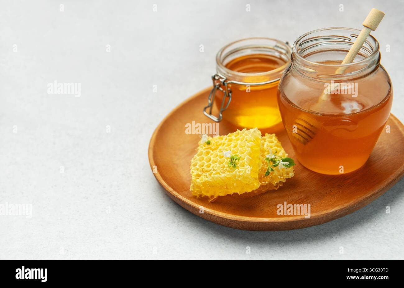 Deux pots remplis de miel doré, de nid d'abeille et de benne reposent sur un plateau en bois, incarnant la douceur naturelle et une vie saine Banque D'Images